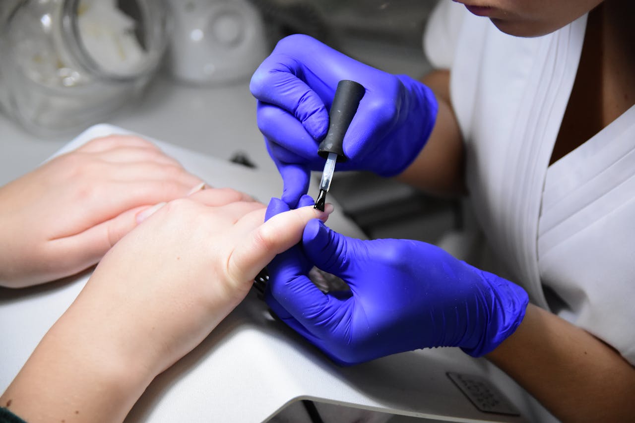embark Close-up of a manicurist applying nail polish wearing purple gloves in a salon.