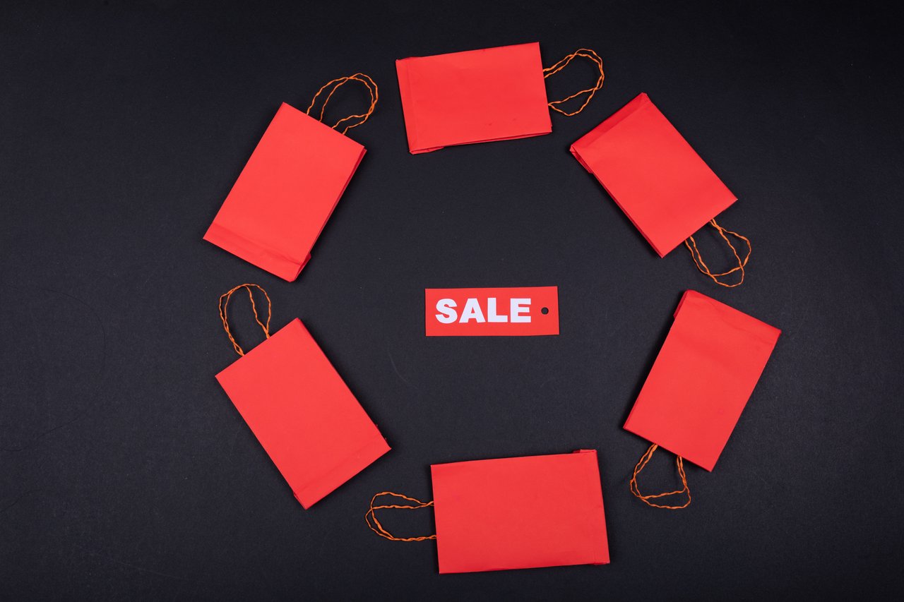 Top view of red paper bags arranged in a circle around a sale tag on a black background.